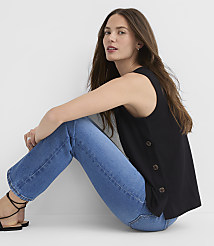 A woman in a black sleeveless top and blue jeans sits against a plain white background. carousel Product Image 2