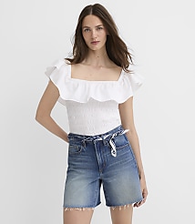 A woman in a white ruffled top and denim shorts stands against a plain white background. carousel Product Image 1