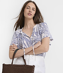A woman in a blue and white patterned blouse and white pants holds a woven brown tote bag in front of a plain white background. carousel Product Image 2