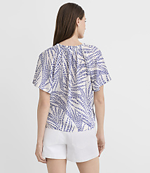 A woman in a white and blue patterned top and white shorts stands against a plain white background. carousel Product Image 3