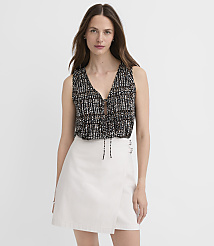 A woman in a patterned top and white skirt stands against a plain white background. carousel Product Image 1