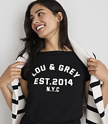 A smiling woman in a black t-shirt with "LOU & GREY EST. 2014 N.Y.C." printed on it, draped with a striped scarf, stands against a plain white background. carousel Product Image 2