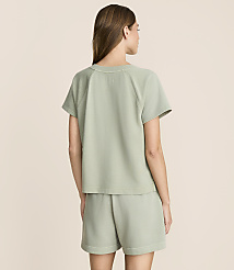A woman in a light green t-shirt and shorts stands against a plain, light beige background. carousel Product Image 3