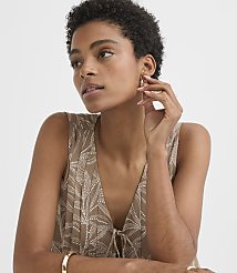 A woman with short, dark hair and a patterned top touches her ear while a plain background surrounds her. carousel Product Image 2