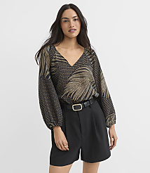 A woman in a patterned blouse and black shorts stands against a plain white background. carousel Product Image 1