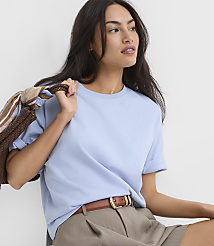 A woman in a light blue t-shirt and brown shorts is holding a striped bag over her shoulder against a plain white background. carousel Product Image 2