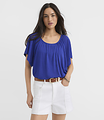 A woman in a blue top and white shorts stands against a plain white background. carousel Product Image 1