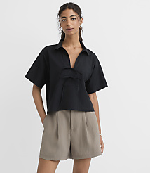 A woman in a black collared shirt and taupe shorts stands against a plain white background. carousel Product Image 1