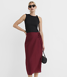 A woman in a black tank top and a maroon wrap skirt poses against a plain white background, holding a small black beaded purse. carousel Product Image 1