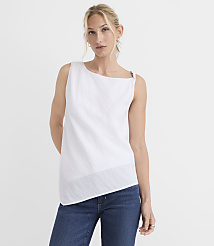 A woman in a white asymmetrical top and blue jeans stands against a plain white background. carousel Product Image 1