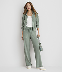 A woman in a sage green loungewear set stands against a plain white background, holding a matching bag. carousel Product Image 1