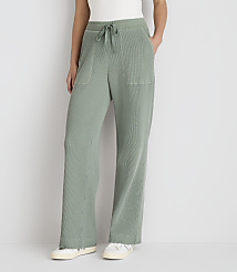 A person stands in front of a plain white background, wearing loose-fitting, light green, ribbed pants with white sneakers. carousel Product Image 2