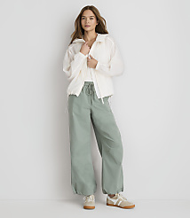 A woman in a white jacket and green pants stands against a plain white background. carousel Product Image 2
