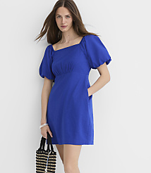 A woman in a blue puff-sleeve dress stands against a plain white background, holding a black and white beaded bag. carousel Product Image 3