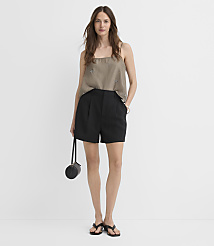 A woman in a taupe camisole and black shorts stands against a plain white background, holding a small black purse. carousel Product Image 1