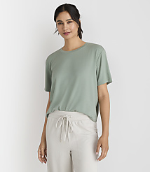 A woman in a green t-shirt and light-colored pants stands against a plain white background. carousel Product Image 1