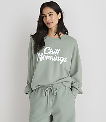 A woman in a light green sweatshirt with \"Chill Mornings\" printed on it stands against a plain white background. carousel Product Image 1