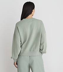 A woman in a light green sweatshirt and pants stands with her back to the camera against a plain white background. carousel Product Image 3