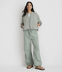 A woman stands in the foreground wearing a sage green bomber jacket and matching wide-leg pants, against a plain white background. carousel Product Image 2