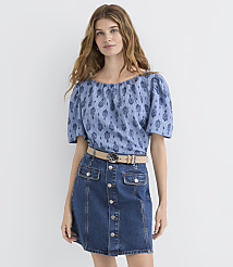 A woman in a blue patterned off-the-shoulder top and a denim skirt stands against a plain white background. carousel Product Image 2