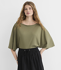 A woman in a green dolman-sleeve shirt and black skirt stands against a plain white background. carousel Product Image 1