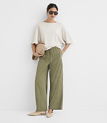 A woman in a cream-colored oversized t-shirt and olive green pinstripe wide-leg pants stands against a plain white background, holding a tan crossbody bag. carousel Product Image 2