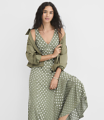 A woman in a polka-dot dress and olive jacket poses against a plain white background. carousel Product Image 1
