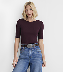 A woman in a maroon ribbed shirt and blue jeans stands against a plain white background. carousel Product Image 1