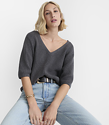 A woman in a dark grey v-neck sweater and light blue jeans sits against a plain white background. carousel Product Image 2