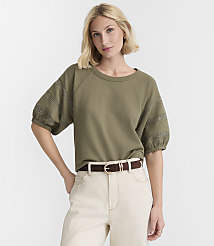 A woman in a green top and cream pants stands against a plain white background. carousel Product Image 2