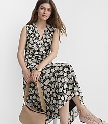 A woman in a floral dress sits on a stool with a light-colored purse on her lap, against a plain white background. carousel Product Image 2