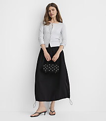 A woman in a light gray cardigan and black skirt stands against a plain white background, holding a small beaded purse. carousel Product Image 2