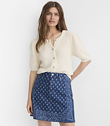 A woman in a cream-colored cardigan and a patterned denim skirt stands against a plain white background. carousel Product Image 1