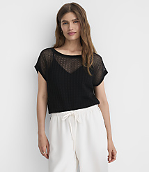 A woman in a black sheer top and white pants stands against a plain white background. carousel Product Image 2