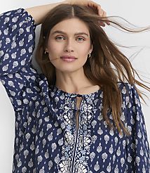A woman with long brown hair and blue eyes, wearing a blue patterned blouse, is captured in a close-up shot against a plain white background. carousel Product Image 1