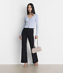 A woman in a light blue cardigan and black flared pants stands with a beige handbag against a plain white background. carousel Product Image 1