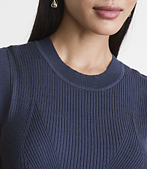 A close-up of a woman's neck and shoulders wearing a navy blue ribbed sweater, with a blurred background. carousel Product Image 4