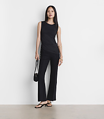 A woman in a black tank top and flared pants stands against a plain white background, holding a small black purse. carousel Product Image 1