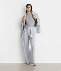 A woman in a grey ribbed top, light blue belted trousers, and a light blue jacket draped over her shoulders stands against a plain white background. carousel Product Image 1