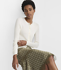 A woman in a cream cardigan and a polka dot skirt sits against a plain white background. carousel Product Image 1
