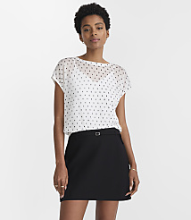 A woman in a white polka dot blouse and black skirt stands against a plain white background. carousel Product Image 1