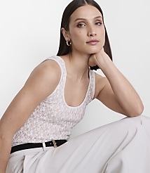 A woman in a white lace tank top and light-colored pants rests her chin on her hand against a plain white background. carousel Product Image 2
