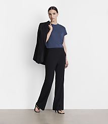 A woman in a blue t-shirt and black pants stands against a white background, with a black blazer draped over her shoulder. carousel Product Image 1