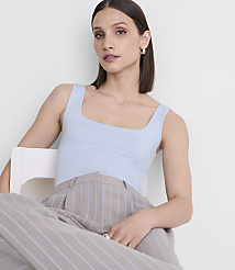 A woman in a light blue tank top and pinstripe pants sits on a white chair against a plain white background. carousel Product Image 2