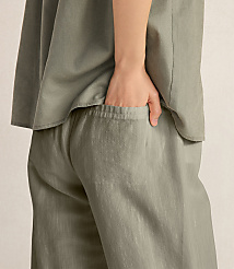 A hand rests in the pocket of loose-fitting, olive-green pants against a plain, light-colored background. carousel Product Image 3