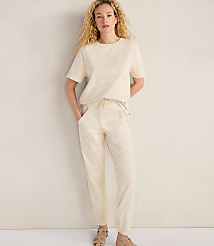 A woman in a cream-colored t-shirt and pants stands against a plain, light-colored wall. carousel Product Image 2