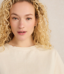A young woman with curly blonde hair and fair skin looks forward against a textured, light-colored background. carousel Product Image 3