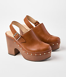 A pair of brown leather clogs with wooden platform soles and gold stud detailing are displayed against a plain white background. carousel Product Image 1