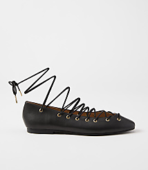 A black leather lace-up ballet flat with gold eyelets rests on a plain white background. carousel Product Image 1