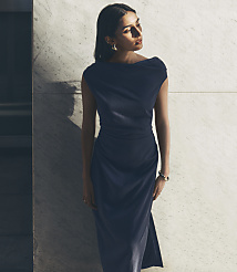 A woman in a dark blue dress stands against a marbled wall. carousel Product Image 6